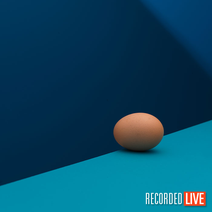 An egg sat on a light blue surface with a juxtaposing blue background